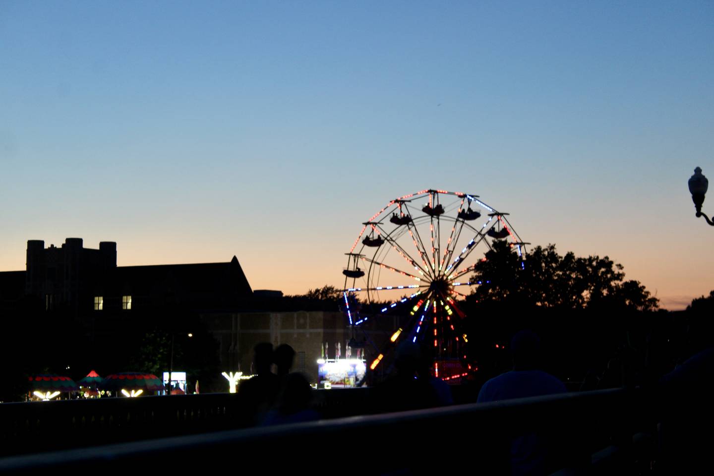 A Ferris wheel turns as sun sets on the Petunia Festival on Sunday. The carnival and midway was set up adjacent to Dixon High School, whose crenelated tower is shown in silhouette.