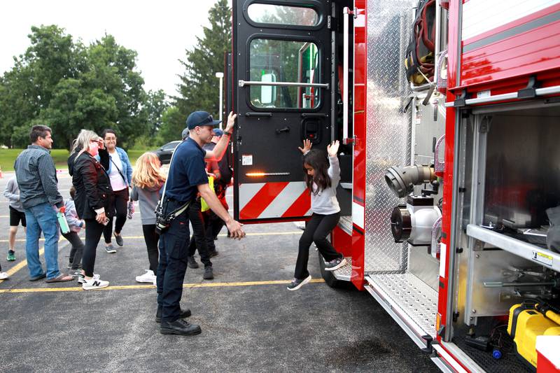 Kaneville Fire Department volunteer firefighter Everett Rutan helps children out of an engine duirng the Kane County Sheriff’s National Night Out in St. Charles on Tuesday, Aug. 6, 2024.