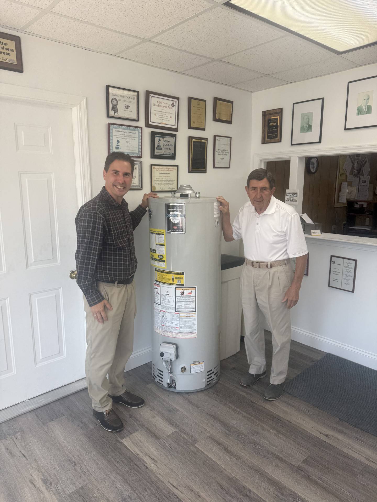 Jake Mahalik. vice president of business at PDM Plumbing, Heating & Cooling in Joliet (left) poses with his father Rudy Mahalik Jr (right), chairman of PDM, near the water cooler in PDM's office. PDM is celebrating its 140th anniversary in 2025.