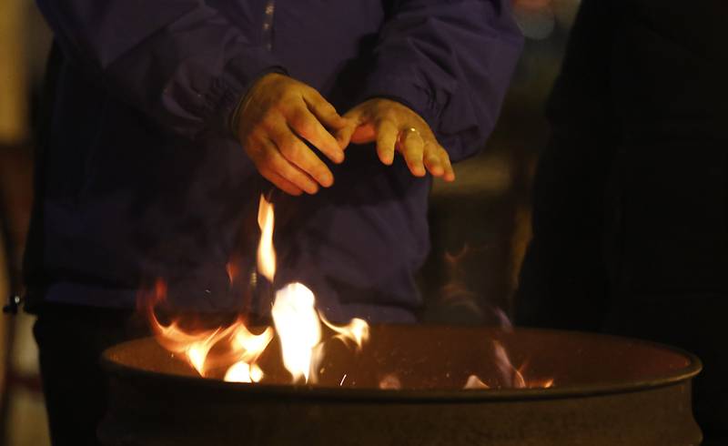 A man warms his hands over a fire during the Lighting of the Square Friday, Nov. 29, 2024, in Woodstock. The annual holiday season event featured brass music, caroling, free doughnuts and cider, food trucks, festive selfie stations and shopping.
