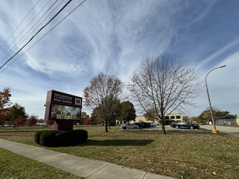 Morris Community High School in Morris during the daytime. The sign out front is surrounded by leaves falling off the trees.