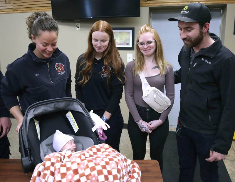 Alicia Dimova, Genoa-Kingston firefighter paramedic, (left) and Haley Stevenson, EMT in training, look at a napping Eleanor Lee Altepeter-Knotts, along with her parents Sammie Altepeter and Brodie Knotts (right) from Kingston Thursday, Nov. 2, 2023, as the baby and her family visit the Genoa-Kingston Fire Department in Genoa. An ambulance crew from the department delivered the baby in the ambulance along the side of the road Sept. 29 when they realized they weren’t going to make it to the hospital in time.