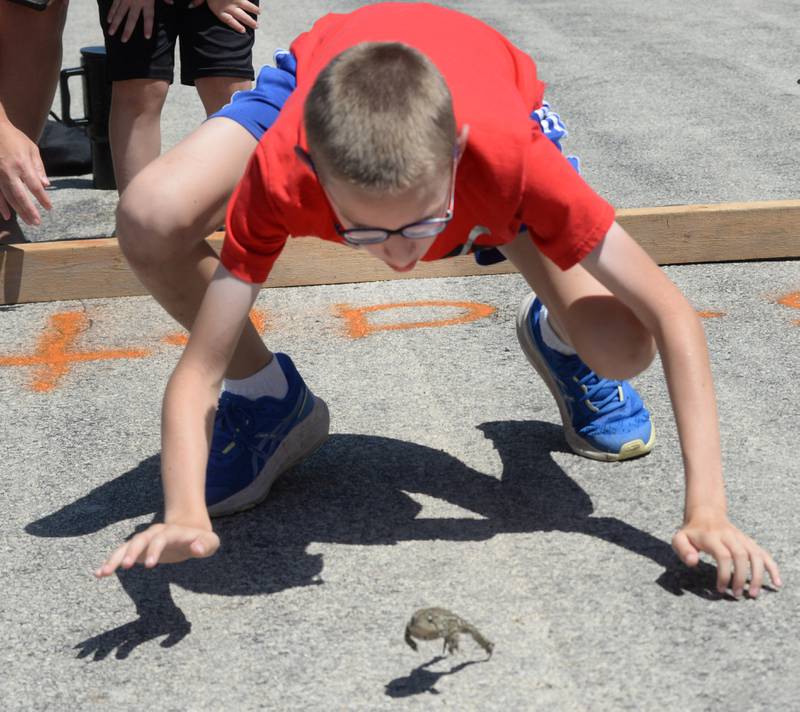 Silas Newman, 12, of Erie, crouches behind "Bill" his toad to encourage the amphibian to hop toward the finish line at the Hooppole Fun Day's Toad Race held Saturday, June 28, 2025 in Hooppole.