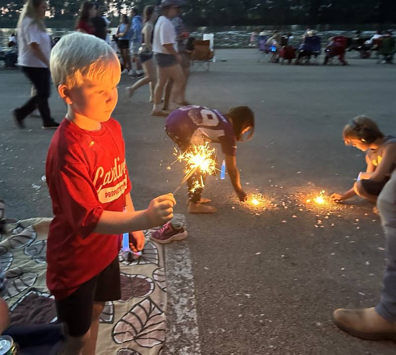 Thatcher Lundy, 6, of Prophetstown, plays with a sparkler as his friends use theirs to burn popcorn kernels as they wait for the fireworks to begin at Prophetstown State Park on Saturday, July 6, 2024.