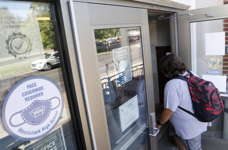 A student enters the building past face mask signs during the first day back to school at Woodstock High School on Monday, Aug. 16, 2021
