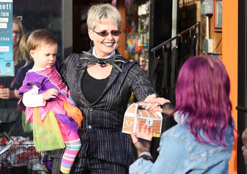 Svetlana Henrikson and Amelia Santiago, 2, from There’s Fun In Store hand out candy in front of the shop Lincoln Highway in downtown DeKalb Thursday, Oct. 27, 2022, during the Spooktacular trick-or-treating event hosted by the DeKalb Chamber of Commerce.