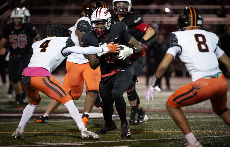 Bradley-Bourbonnais' Dachaun Anderson, center, carries the ball as Dekalb's Kirk Johnson, left, looks to make the tackle in a game on Friday, October, 10, 2025.