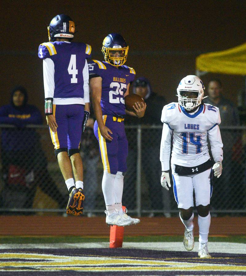 Wauconda's Connor Vanselow (25) leaps to celebrate his touchdown with teammate Brock Pfeiffer (4) as Lakes' Prodive Matumona-Nzama looks on during Friday’s football game in Wauconda.