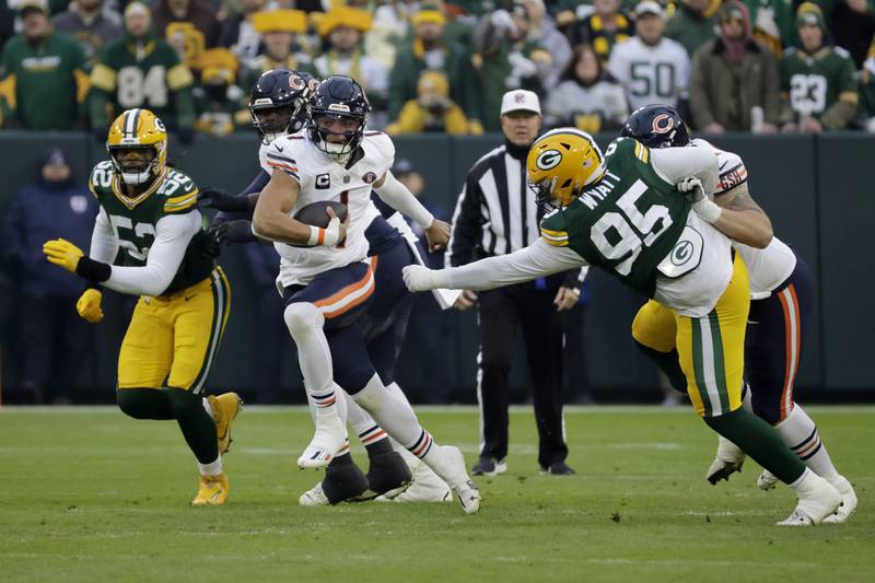 Chicago Bears quarterback Justin Fields runs between Green Bay Packers linebacker Rashan Gary (52) and defensive tackle Devonte Wyatt (95) during the first half Sunday, Jan. 7, 2024, in Green Bay, Wis.