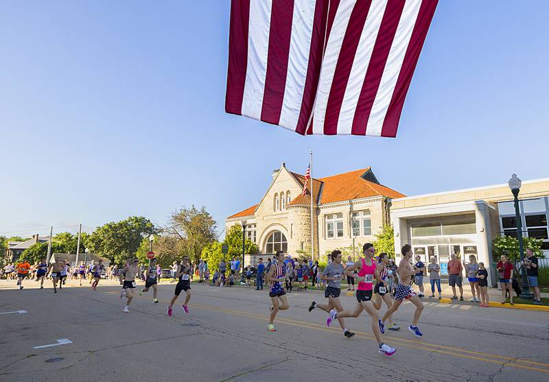 The lead runners pass under a giant American flag put on display by the Dixon Fire Department on Saturday, July 6, 2024, during the Reagan Run 5K.