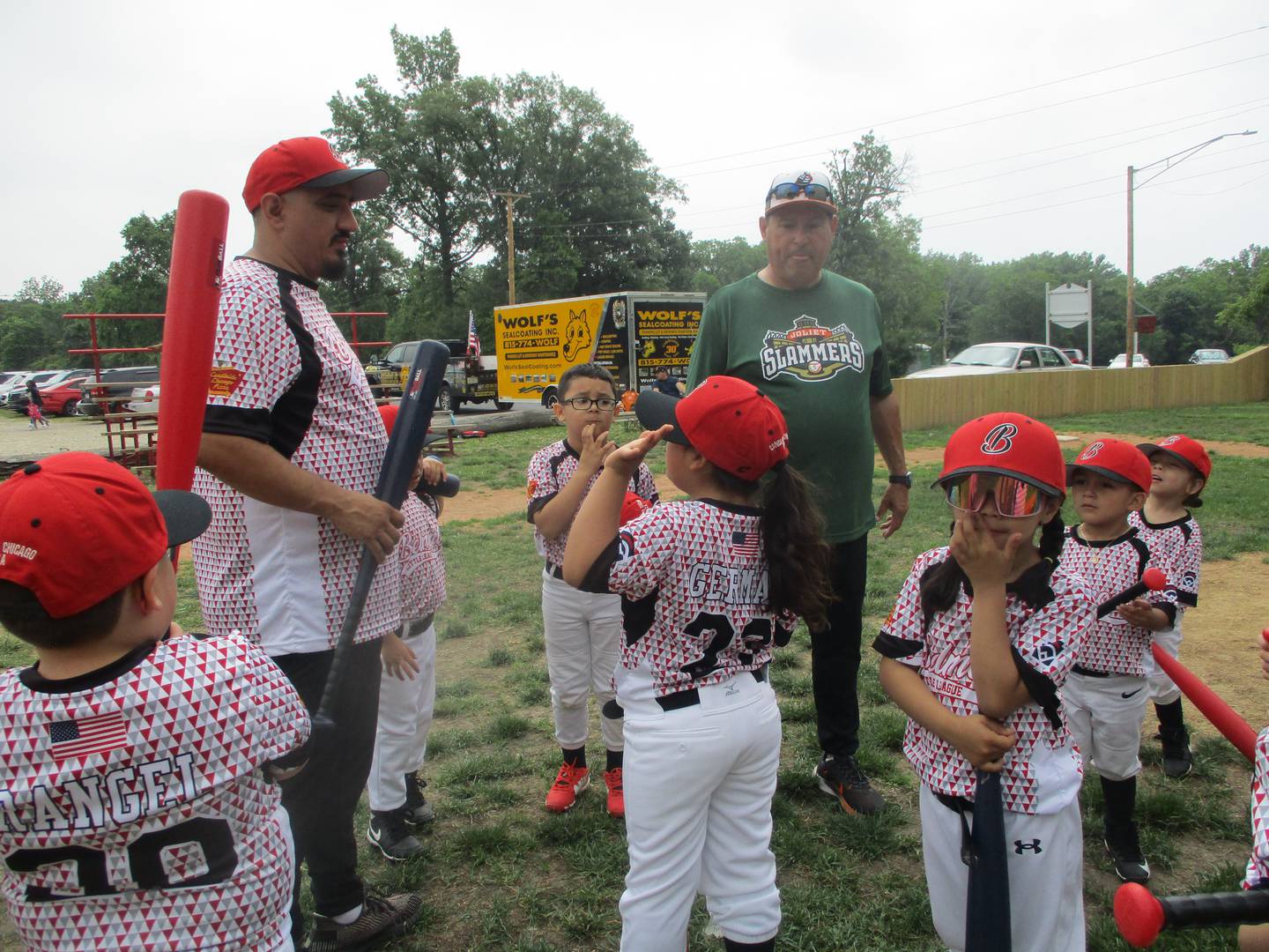 Belmont Little Leaguers gather around Coach Adrian Ulloa (left) and Slammers Bench Coach Ron Biga (right) for instruction on their T-Ball field in Joliet. June 14, 2025