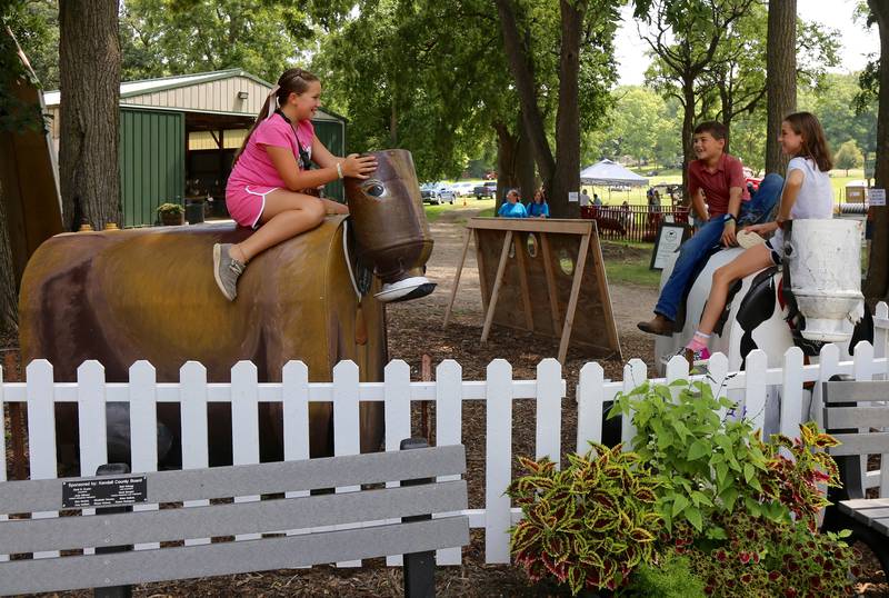 Adelynn Landers, August Scwartz and Nessa Carlson (from left) play on the metals cows at the Kendall County Fair in Yorkville on Saturday, Aug. 2, 2025.