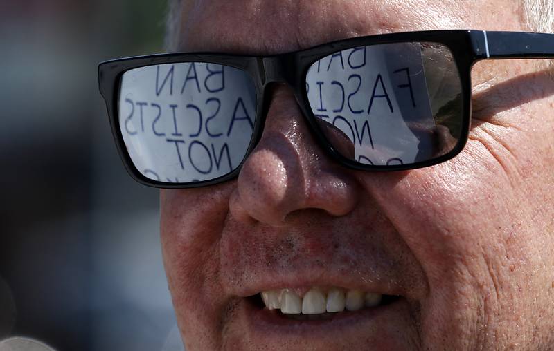 A protest sign is reflected in glasses that Bob Janz of McHenry is wearing on Friday, June 20, 2025, on Route 31 in front of the McHenry Public Library during a Save Our Libraries Protest hosted by Indivisible McHenry County to draw attention to cuts to the nation’s libraries by the Trump administration.