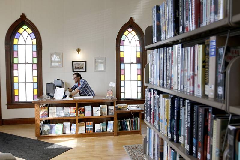 Josh Stevens, the head librarian at Hebron Public Library, looks for a book in the computer catalog on Thursday, Aug. 25, 2022, at the library in Hebron. Stevens is a teacher during the day and the librarian for the privately funded Hebron library at night.