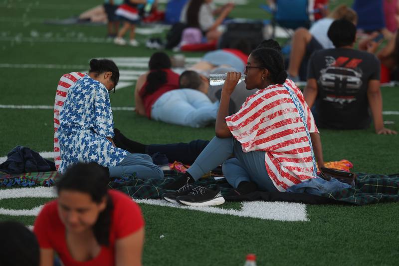 A couple sits on the field wearing matching festive shirts before the start of the fireworks at Joliet Memorial Stadium in on Thursday July 4, 2024.