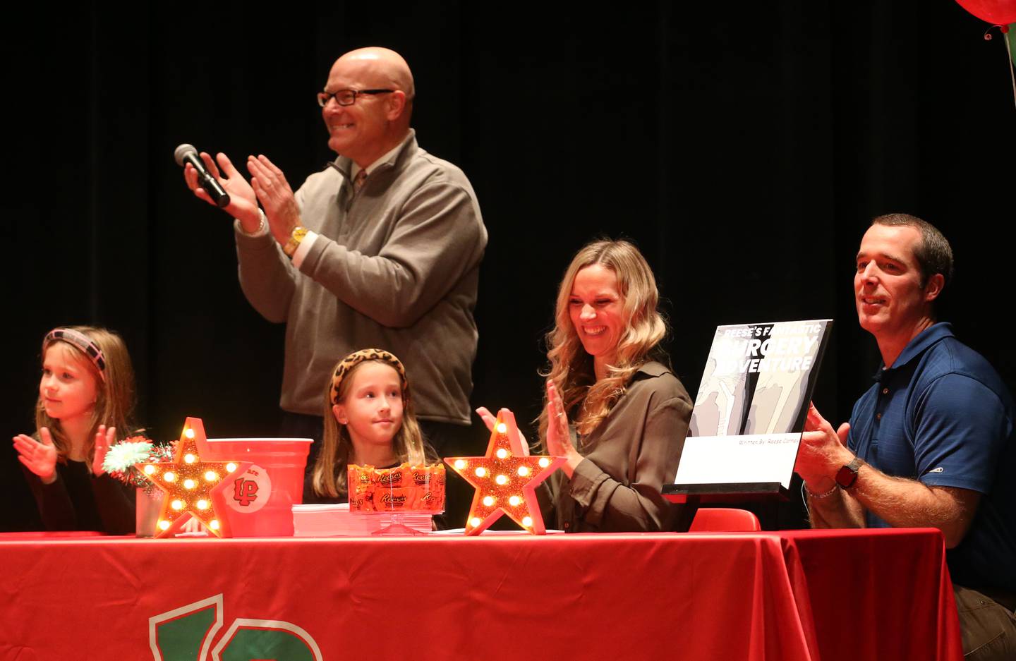 La Salle-Peru Township High School superintendent Steve Wrobleski (back) applauds with the Carney family (front from left) Avery, Reese, Amy and Pat unveil a new book that Reese wrote titled "Reeses Fantastic Surgery Adventure" on Monday, Nov. 6, 2023 at Matthiessen Auditorium.