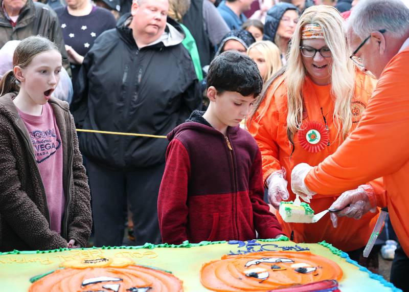 Finley McDonald, (left) honorable mention winner in the theme contest, can’t believe the size of the piece of cake that Harrison Rowland, winner of the theme contest, and Brandi Voigt, theme director of the Pumpkin Fest Committee, cut during the cake cutting Wednesday, Oct. 25, 2023, on North Maple Street adjacent to the DeKalb County Courthouse during the Sycamore Pumpkin Festival.