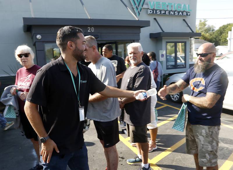 A.J. Sullins  of Vertical Dispensary, hands out water to people wait in line to see former Bears quarterback Jim McMahon during the grand opening of the Vertical Dispensary on Saturday, Sept. 30, 2023, in Cary. The dispensary has been open for about a month.