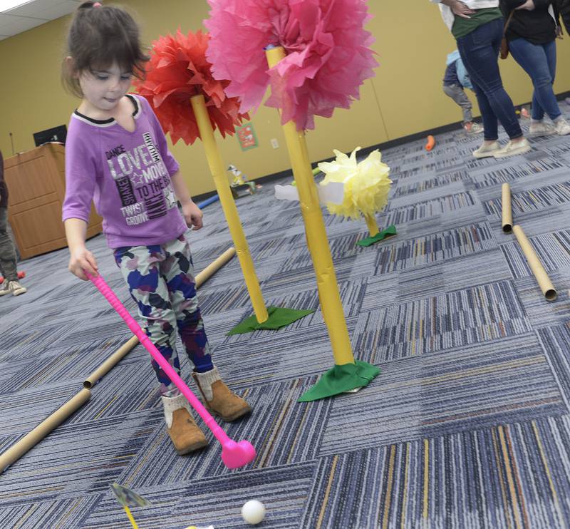 Brinley Stebbins tries a one-handed putt Thursday, March 7, 2024, at the Reddick Library in Ottawa during a special Dr. Seuss miniature golf outing to celebrate the author’s recent birthday.