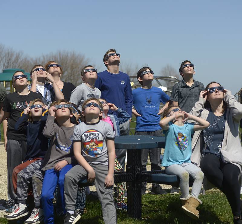 Students and faculty gather Monday, April 8, 2024, on the playground at Deer Park School in rural Ottawa to view the partial solar eclipse.