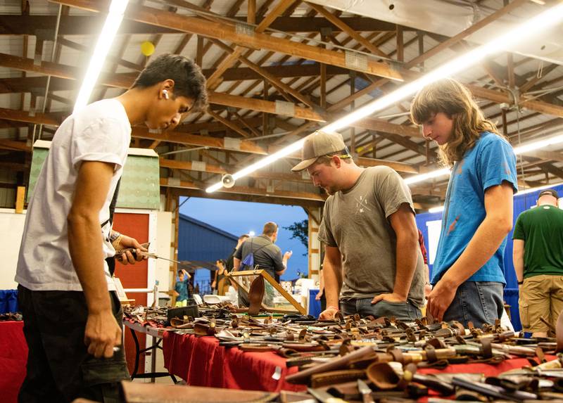 Jenkyn Ledle of Wis. (middle) and Devin Abraham of Hebron (right) look at the Titan International Knives table ran by Hakam Jamil of Lakewood during the 75th Anniversary of the McHenry County Fair in Woodstock on Friday, August 4, 2023.