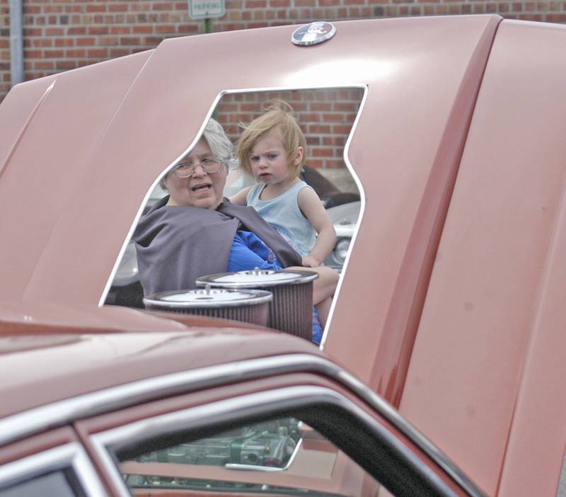 Lookers are framed in a car's hood opening. Sterling Main Street's 12th Annual Car Show took place at the Sterling Marketplace on Sunday, May 4th, 2025.