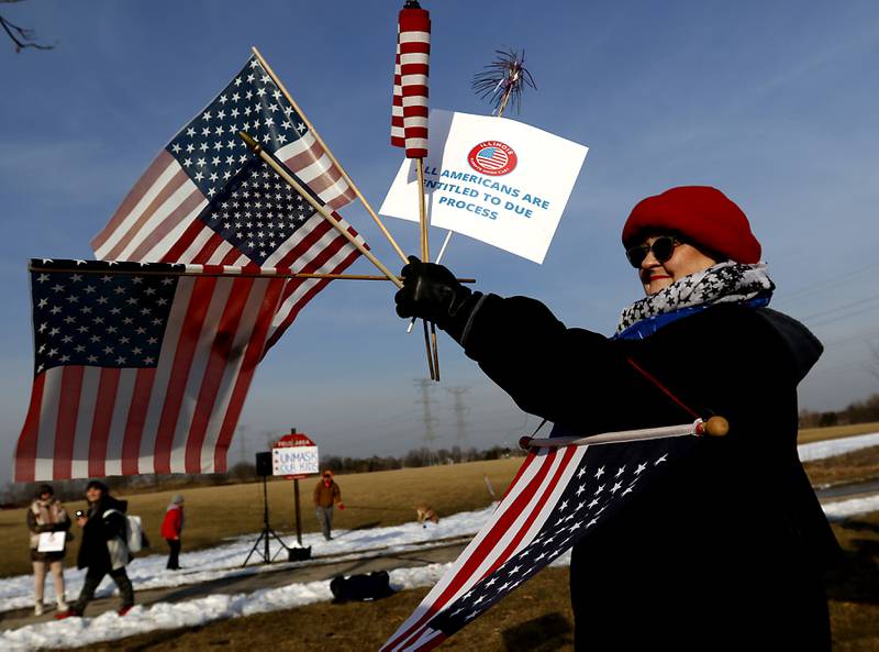 Nancy Swart holds up a sign and flags during a Cary School District 26 anti-mask rally Tuesday, Feb. 15, 2022, along Three Oaks Road at Cary-Grove Park. The event was attend by about 100 people and organized by the Illinois Parents Union Cary.