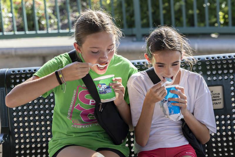Jane Oprian (left), 11, digs into her watermelon-pina colada-mango Kona Ice while Charlotte Kelly, 10, chomps on her blue raspberry-cotton candy-pina colada treat Wednesday, July 23, 2025. The two were keeping cool with the icy drinks at a sweltering Dixon City Market.