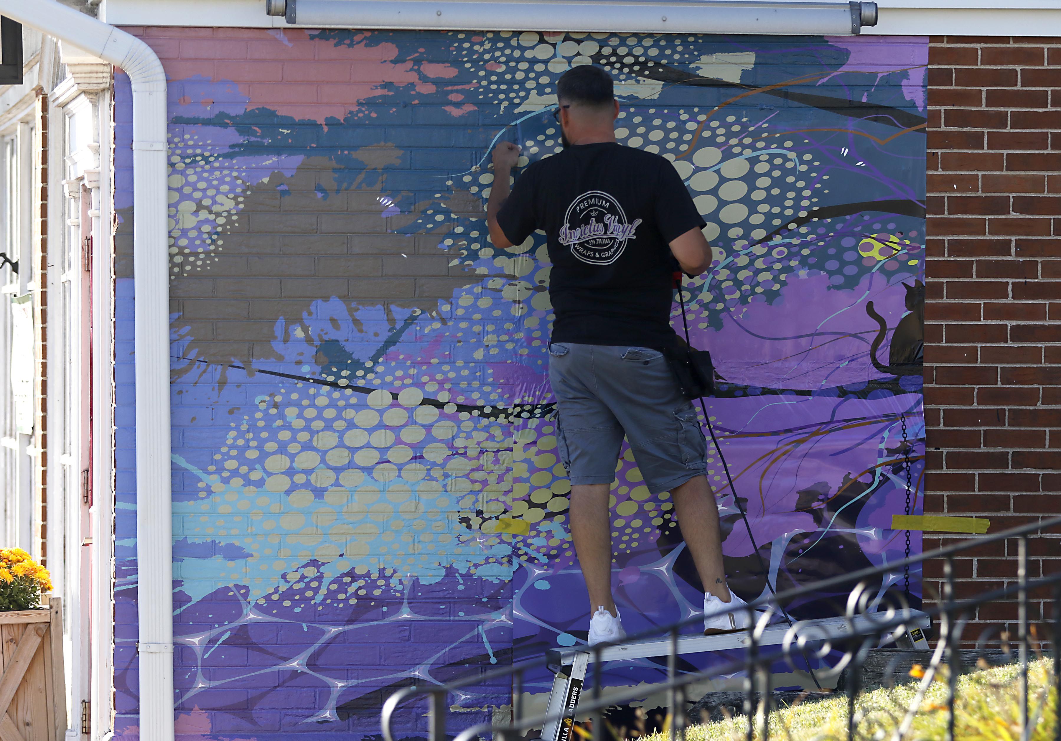 Mike Suchowski, of Invictus Vinyl, instals a new mural on Monday, Sept 15, 2025, on the side of a building at 3430 West Elm Street in McHenry.