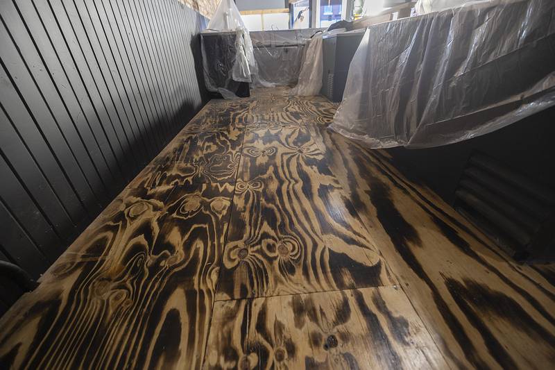 The floor is being treated with a technique that uses a torch to expose and condition the wood grain.