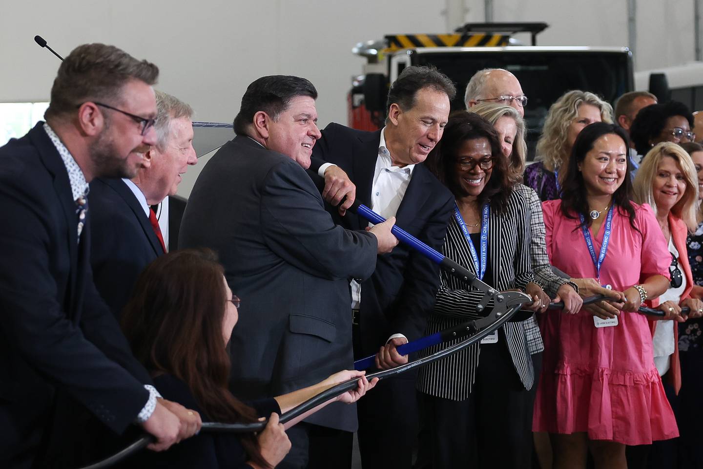 Governor JB Pritzker, center left, and Marc Bedard, CEO of Lion Electric, cut an electric cord in place of a ceremonial ribbon at the grand opening of the Lion Electric manufacturing facility on Friday, July 21st, 2023 in Joliet.