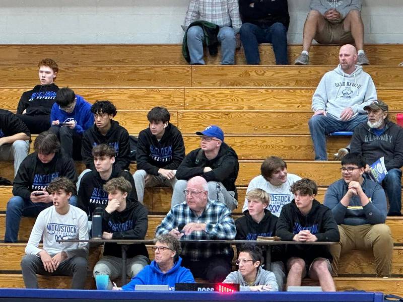 Members of Woodstock's boys basketball program sit with PA announcer Jack Darby  (plaid shirt) during a JV basketball game.