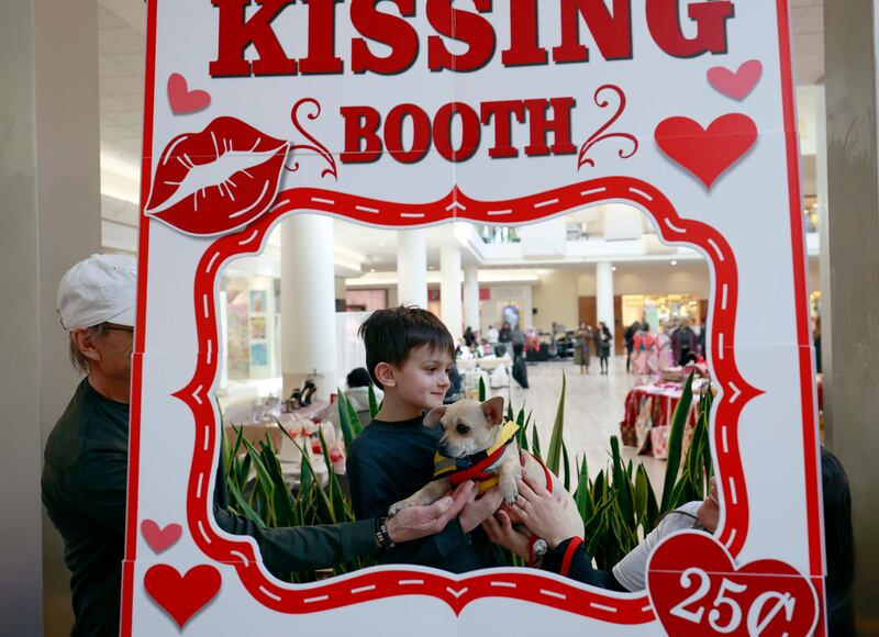 Five-year-old Isaac Brennan of Naperville gets a little help as he poses with a canine friend at the SAINRescue.org doggie kissing booth at Yorktown Center Saturday, Feb. 7, 2026 in Lombard.