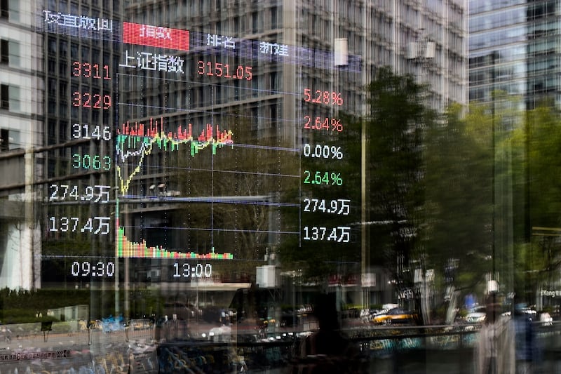 Pedestrian and office buildings are reflected on a brokerage house's window as an electronic board displays Shanghai shares trading index in the Central Business District, in Beijing, Wednesday, April 9, 2025. (AP Photo/Andy Wong)