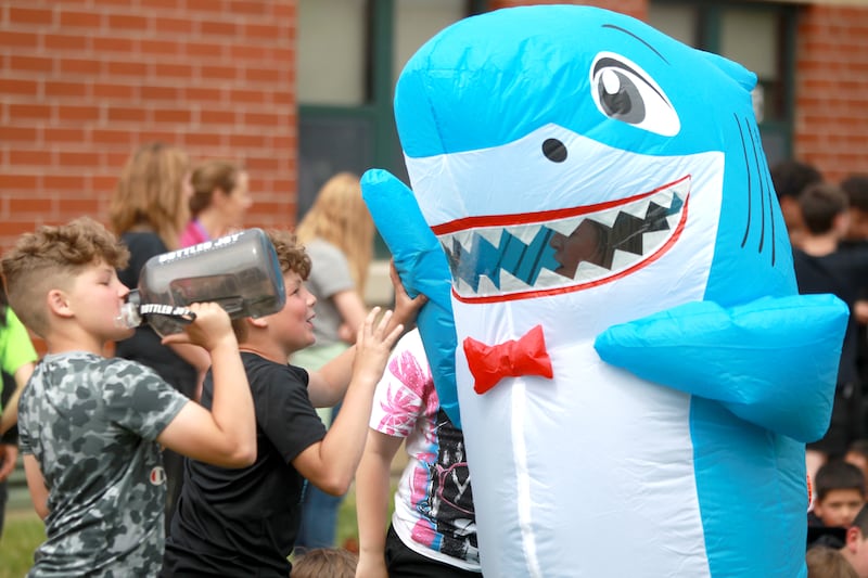 Courtney Baker, dressed in a shark costume, high-fives students at Emily G. Johns Elementary School in Plano after teachers and staff members surprised students with an inflatables race on Tuesday, May 27. 2025 to celebrate the end of the school year.