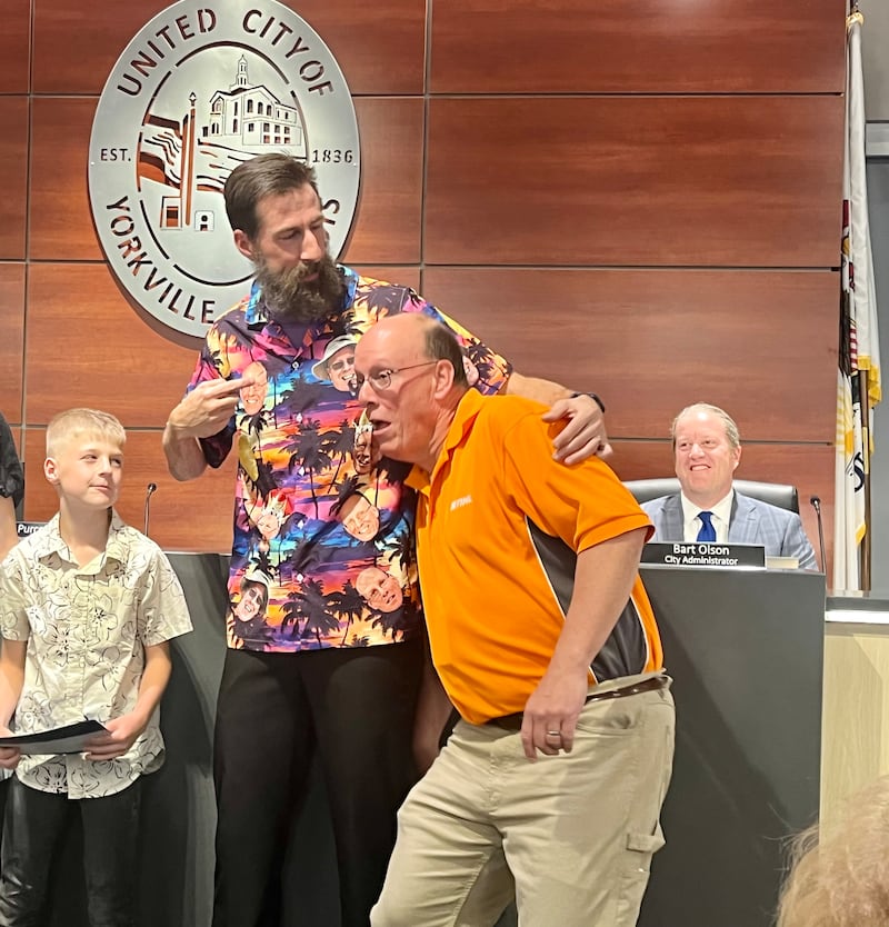 After repeating the oath of office, read aloud by his son, adlerman Matt Marek embraces Mayor John Purcell. In homage to the mayor's predilection for tropical apparel, Marek wore a Hawaiian shirt with photos of the mayor's face spotted across.