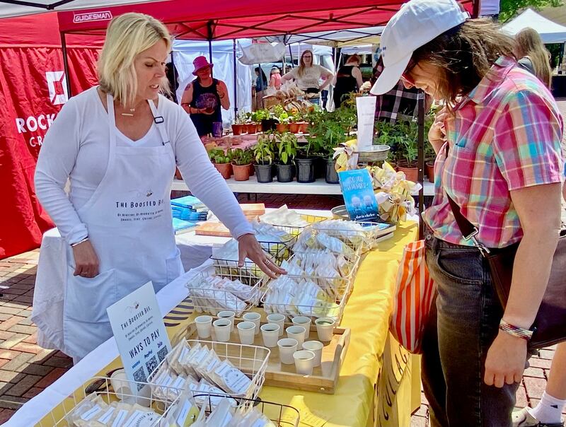 Davis Ehrler (left) talks about her business The Boosted Bee which offers protein coffee, tea and drink samples with a customer at the opening day of the DeKalb farmers market on Thursday, June 5, 2025, in Van Buer Plaza in downtown DeKalb. The market opened its 30th year Thursday.