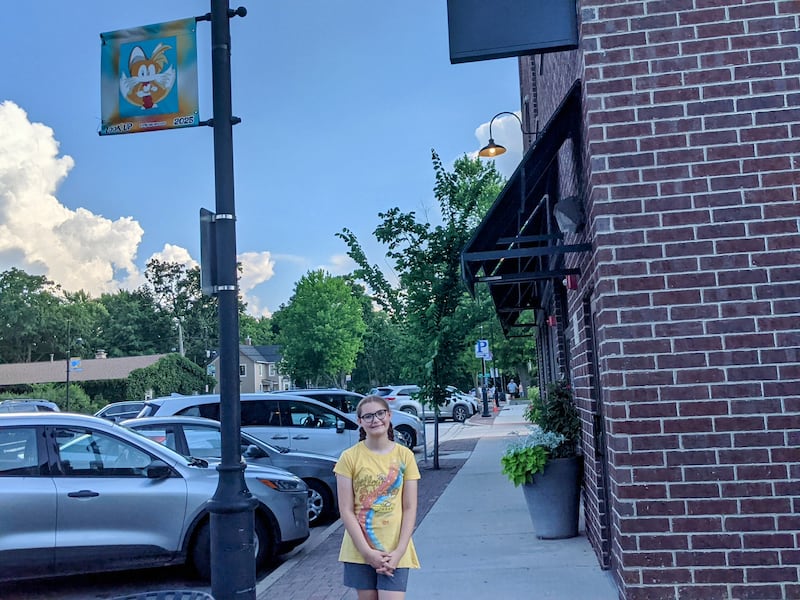 Evelyn Stark, 11, stands next to the banner she made as part of the Look Up Oswego banner program.