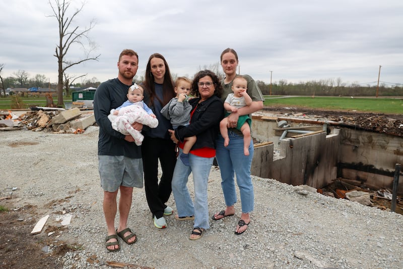 Lisa Gerth, second adult from right, stands with her son and daughter-in-law, Mitchell and Abigail Gerth, at left, with their children Everett, almost 2, and Elowyn, 4 months, as well as close friend and neighbor Erin Boerschig, right, and her 8-month-old son Sawyer, on April 15, 2026, outside the basement where they sheltered during the March 10 tornado that hit Aroma Township.