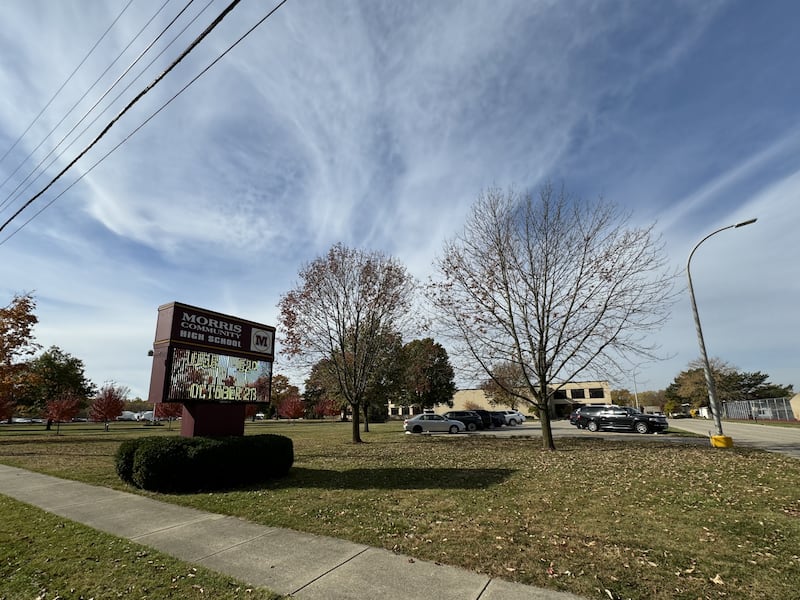 Morris Community High School in Morris during the daytime. The sign out front is surrounded by leaves falling off the trees.