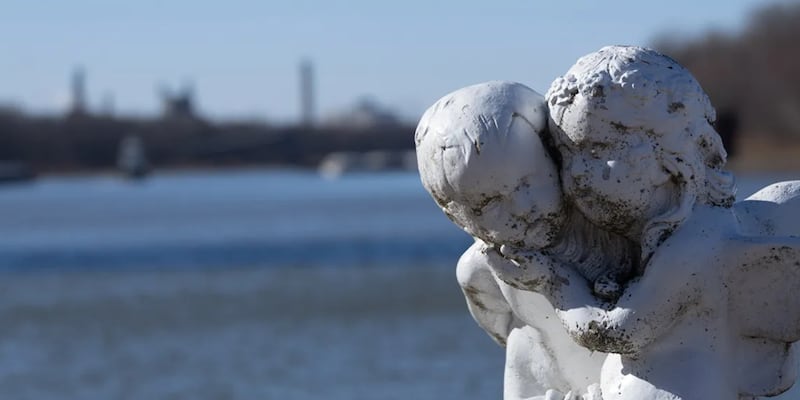 A statue of two angels showing the consequences of air pollution is seen with their backs to the Illinois River and the Powerton coal plant.