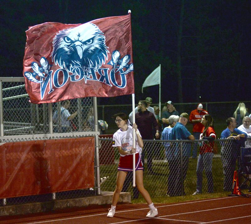 An Oregon cheerleader runs with an Oregon flag during the varsity football game against Genoa-Kingston on Friday, Sept. 13, 2024 at Landers-Loomis Field in Oregon.
