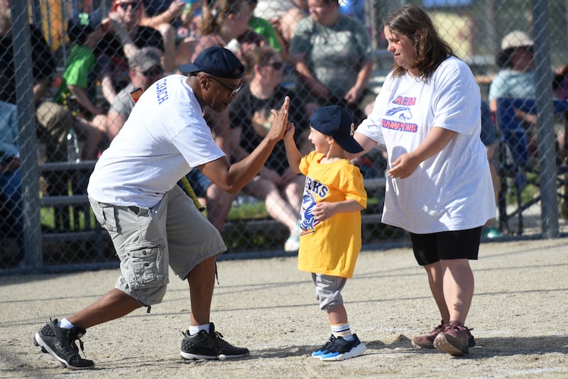 Carson Jacobson, 4, of Chebanse, center, high fives coach Marlow Jones, left, while his mother, coach Heather Jacobson, helps him cross home plate during an ACBA Champions League game at Bishop McNamara Saturday, June 13, 2026.