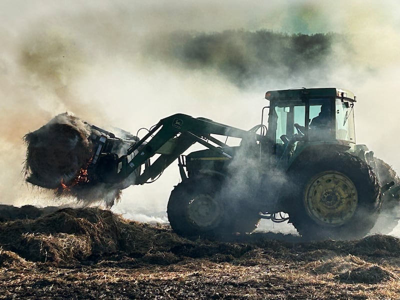 Firefighters from several departments responded to a field and hay bale fire at a farm on West Pines Road between Polo and Oregon on Monday, Feb. 23, 2026. Here, a farmer uses a tractor to carry one of the burning bales out to an open area where firefighters could extinguish it.