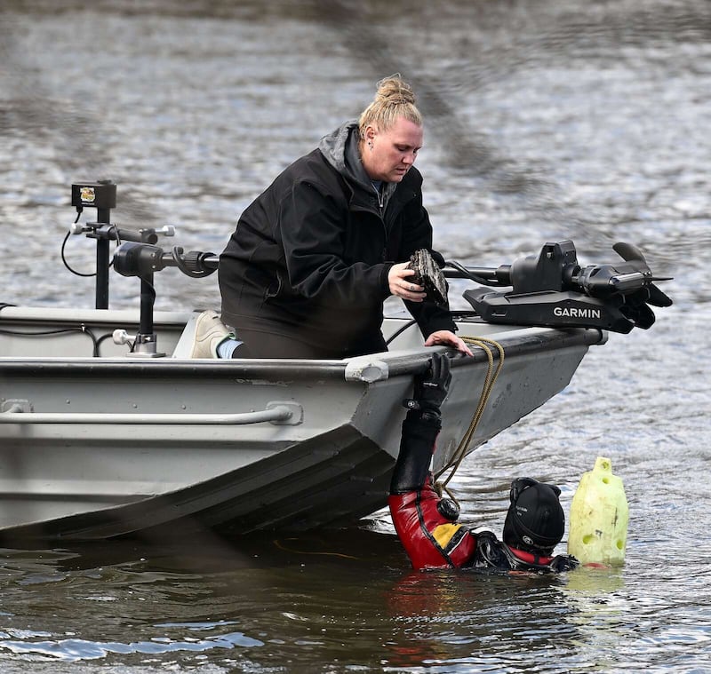 Diver Mike McFerron handed debris, believed to be from a submerged car in the Fox River, to Lindsay Bussick of Chaos Divers on Monday. They were searching for clues related to a cold case from 1983 that the Elgin Police Department is investigating.