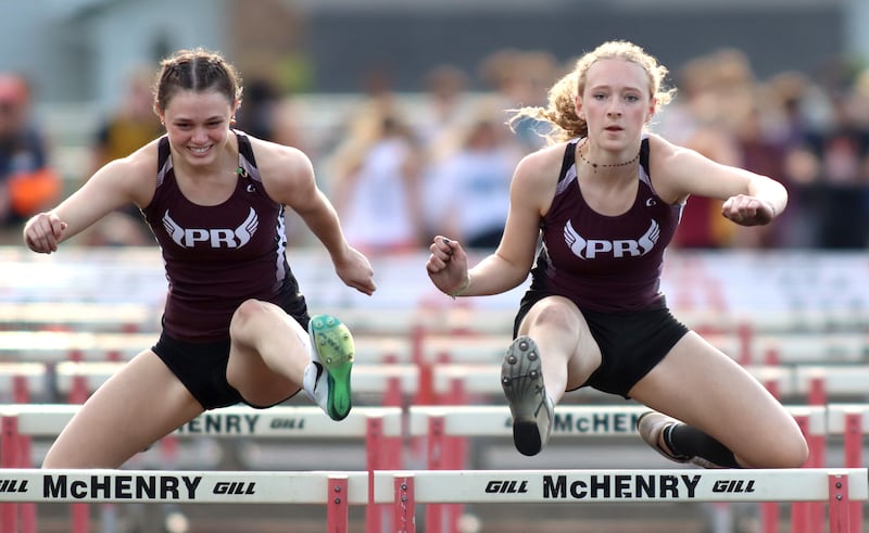Prairie Ridge teammates Marta McCarthy, left, and Leah Berning  compete in the 100-meter hurdles during the McHenry County Track and Field Meet at McCracken Field on Thursday, April 24, 2025, in McHenry