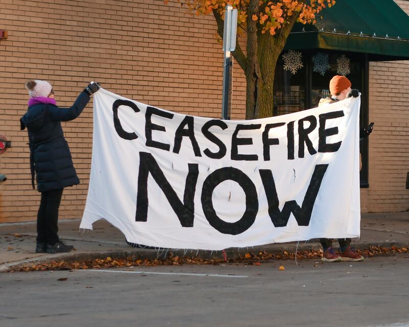 Tom Callahan, right, and his mom Jane Callahan of Downers Grove hold at Ceasefire Now banner relating to the Israel and Palestine war during the Grove Express 5k race held in downtown Downers Grove on Thursday Nov. 23, 2023.