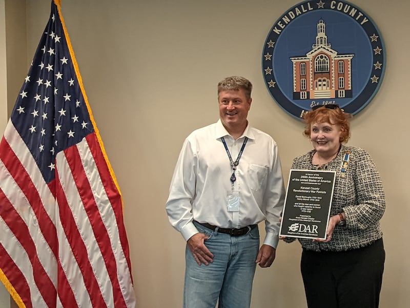 Kendall County Board Chairman Matt Kellogg, left, stands with Johanna Byram, historian with the Amos Kendall chapter of the Daughters of the American Revolution, who presented a plaque recognizing Revolutionary War patriots Daniel Burroughs and Henry Misner at the June 16 Kendall County Board meeting.