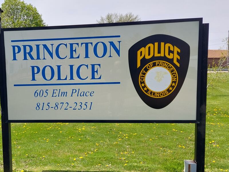 Princeton officer Erik Sorenson watches as K9 officer Gus poses in front of the Princeton Police Department sign.
