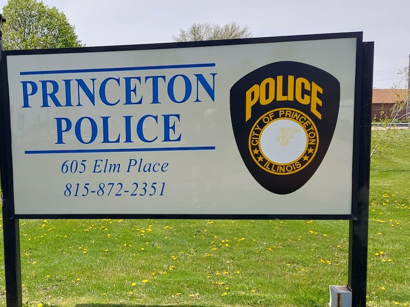 Princeton officer Erik Sorenson watches as K9 officer Gus poses in front of the Princeton Police Department sign.